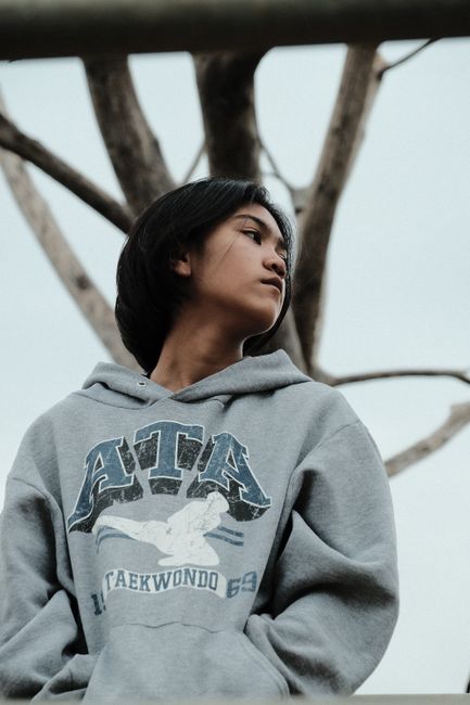 Casual young woman in hoodie looking away thoughtfully outdoors by a bare tree.