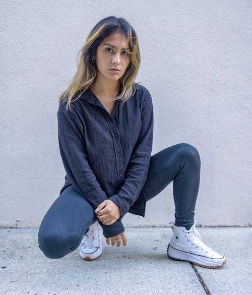 Young Woman in a Casual Outfit Crouching in front of a Wall on a Pavement 
