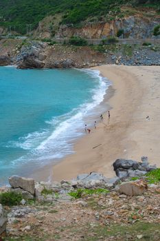A beautiful beach scene with people walking along the golden sand and turquoise sea.