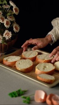 Hands arranging freshly cut bread slices on a baking tray with flowers nearby.