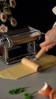 A close-up of rolling fresh pasta dough with a machine in a kitchen setting.