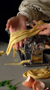 Homemade pasta being carefully crafted with a pasta machine by a woman in the kitchen.