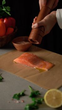 Close-up of a salmon fillet being seasoned with pepper, garnished with fresh herbs.