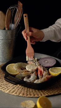 Chef preparing gourmet seafood with prawns and fresh ingredients in a cast iron skillet, ready to serve.