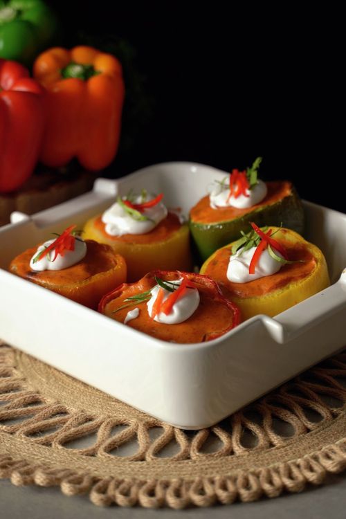 Free Colorful stuffed bell peppers served in a white dish, topped with cream and herbs. Stock Photo