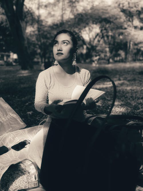 Black and White Photo of a Woman Standing in a Park with an Open Book 