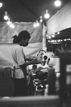 A focused street vendor in a night market booth, captured in classic black and white.