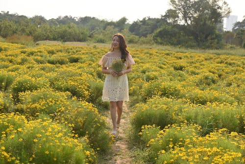 Young Woman Walking on a Meadow and Holding Flowers