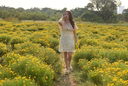 Young Woman Walking on a Meadow and Holding Flowers