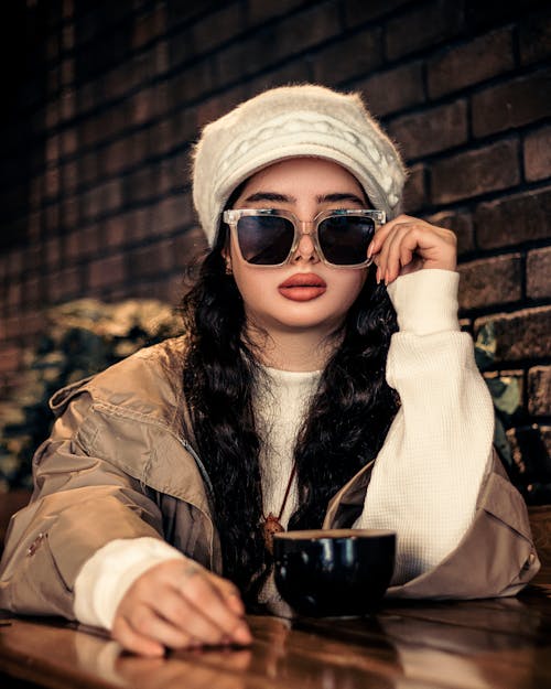 Woman in Hat and Sunglasses Sitting by Table at Cafe
