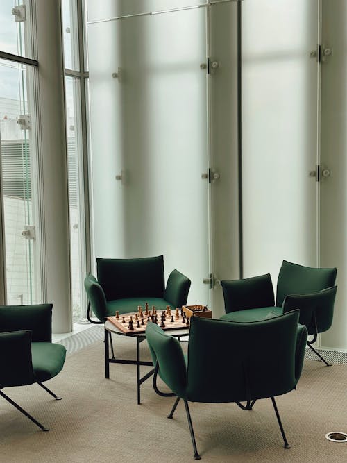 Green Armchairs Arranged Around a Chessboard on a Coffee Table in a Corner Room