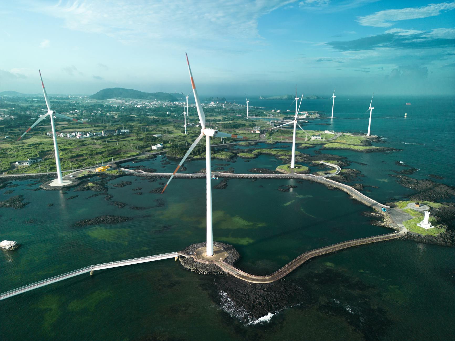 Aerial photo of wind turbines set against a coastal landscape with bright blue waters.