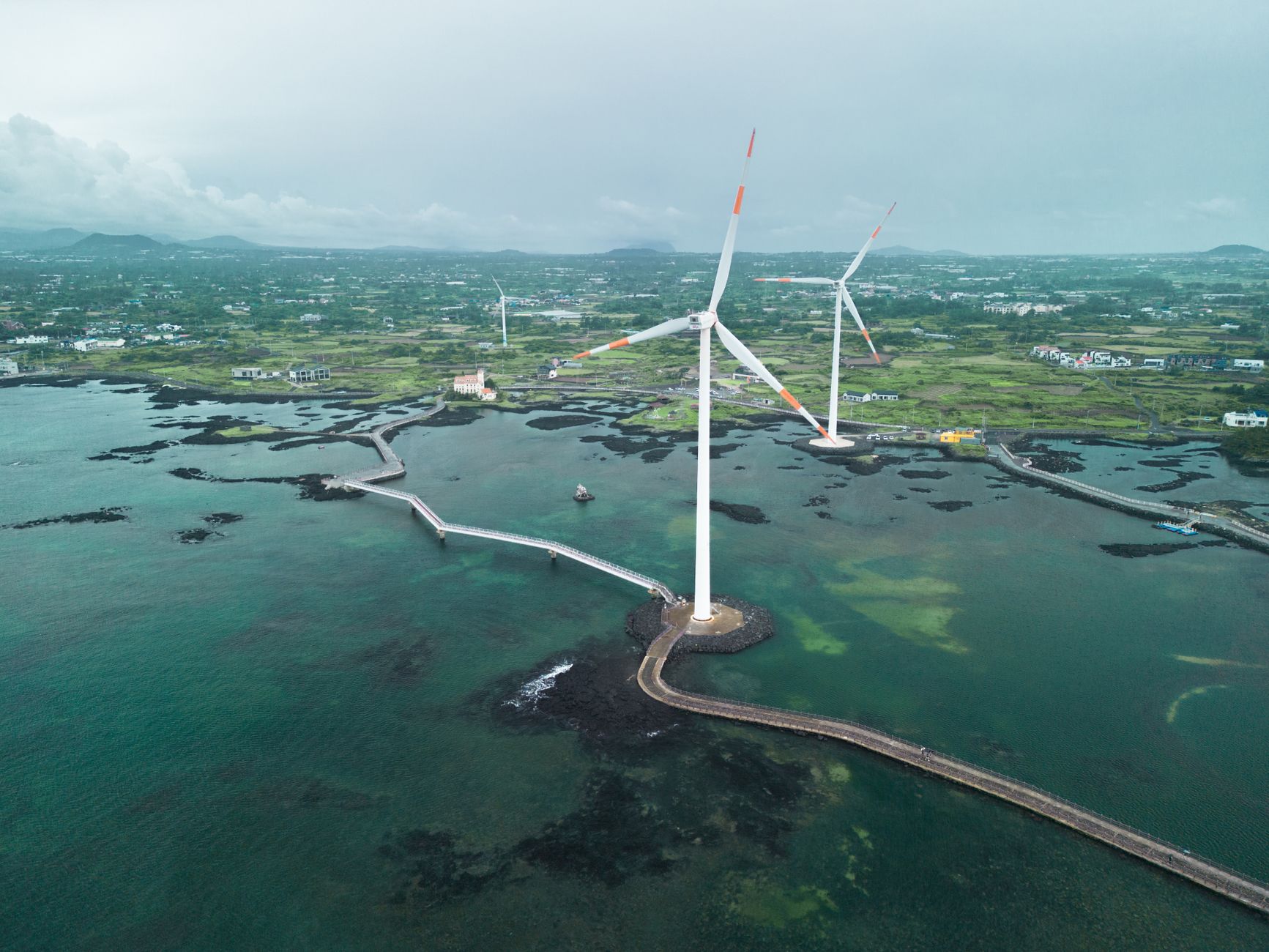 Scenic aerial shot of wind turbines along Jeju's coast, showcasing renewable energy.