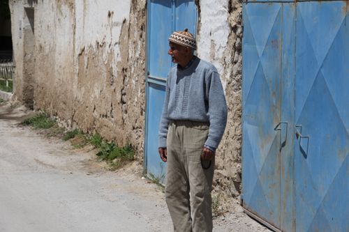 Free Senior man standing in rural setting by a blue metal gate with worn walls. Stock Photo