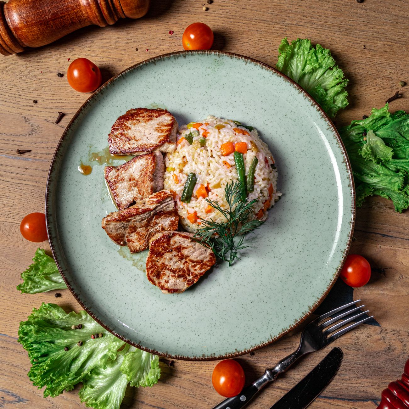 Top view of sliced pork chops with vegetable rice on a rustic table.
