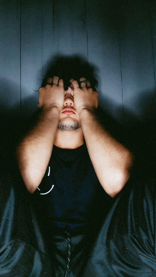 Free Portrait of a young man sitting with hands on face, evoking an introspective mood. Stock Photo