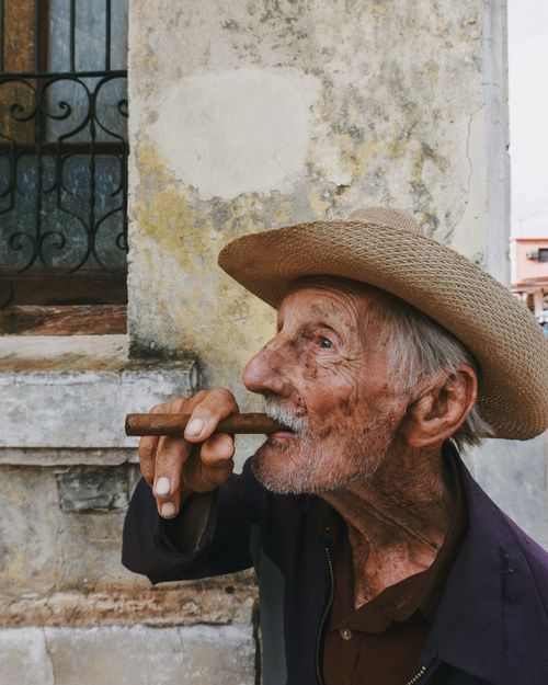 Free Portrait of a senior man smoking a cigar against a rustic wall with a textured surface. Stock Photo