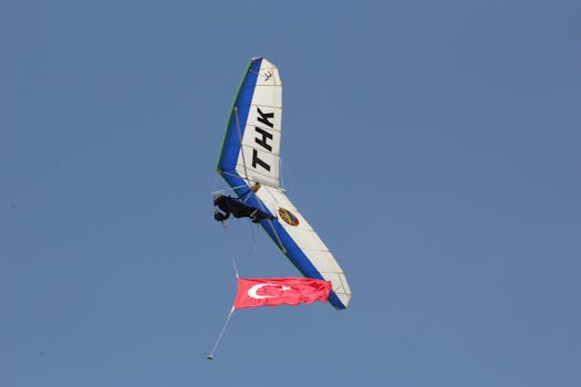 Hang glider flying against clear sky, displaying the Turkish flag. Perfect capture of aerial sport.