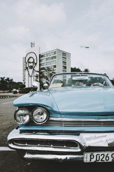 Front view of a classic blue car in Havana with iconic Cuban architecture in the backdrop.