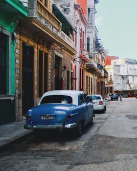 Classic blue vintage car parked on a vibrant Havana street with colorful buildings.