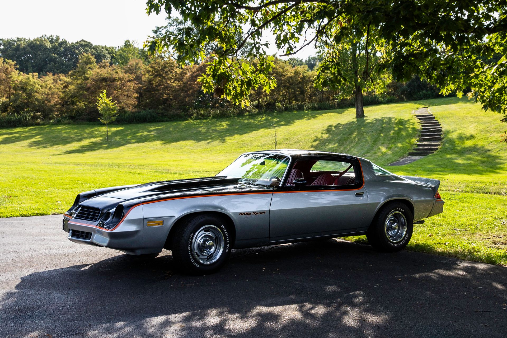 A silver 1979 Chevrolet Camaro parked on a sunny day in a lush green park.