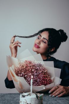 Portrait of a young woman holding a bouquet and a candlelit cake, exuding elegance and warmth.