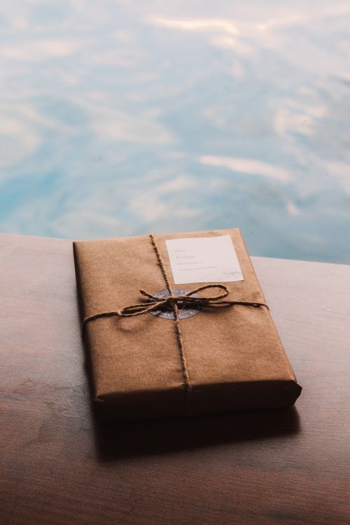 Free Brown paper gift package tied with twine placed on a wooden surface by the water. Stock Photo