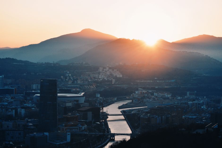 Una impresionante vista aérea de Bilbao con el atardecer proyectando un cálido resplandor sobre la ciudad y las colinas circundantes.