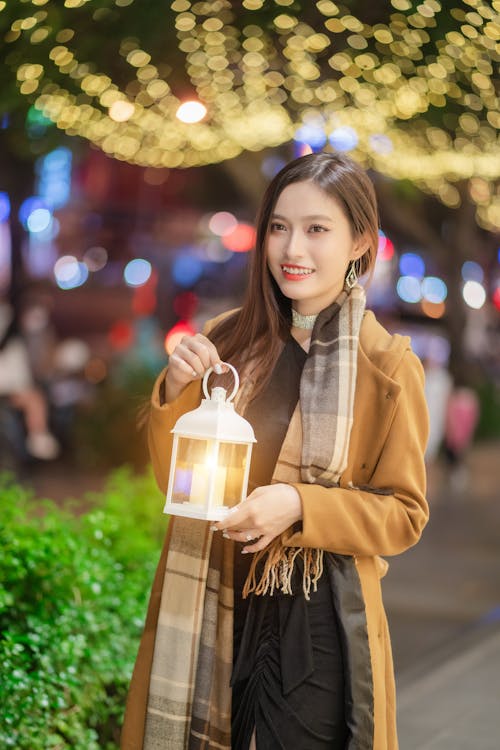 Smiling Woman in Coat Standing with Lantern at Night