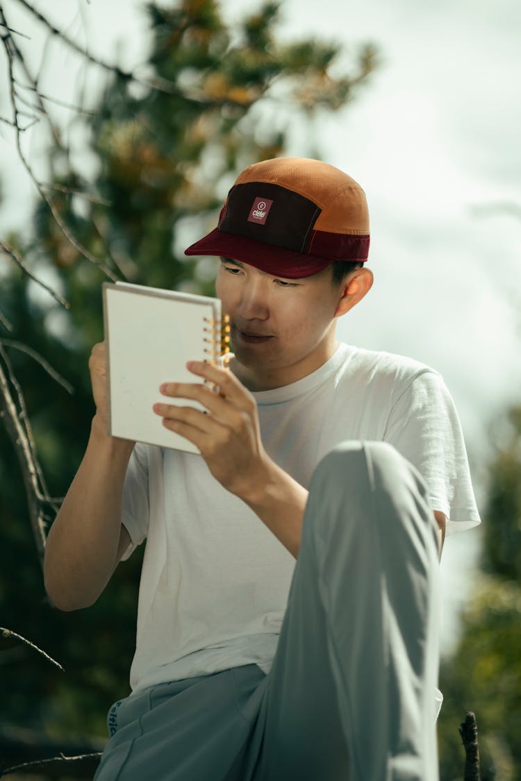 Man In Cap Sitting And Writing In Notebook