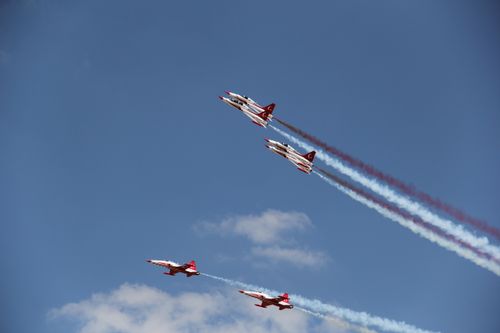 Free Four military jets perform aerobatic maneuvers, leaving colored smoke trails against a clear blue sky. Stock Photo