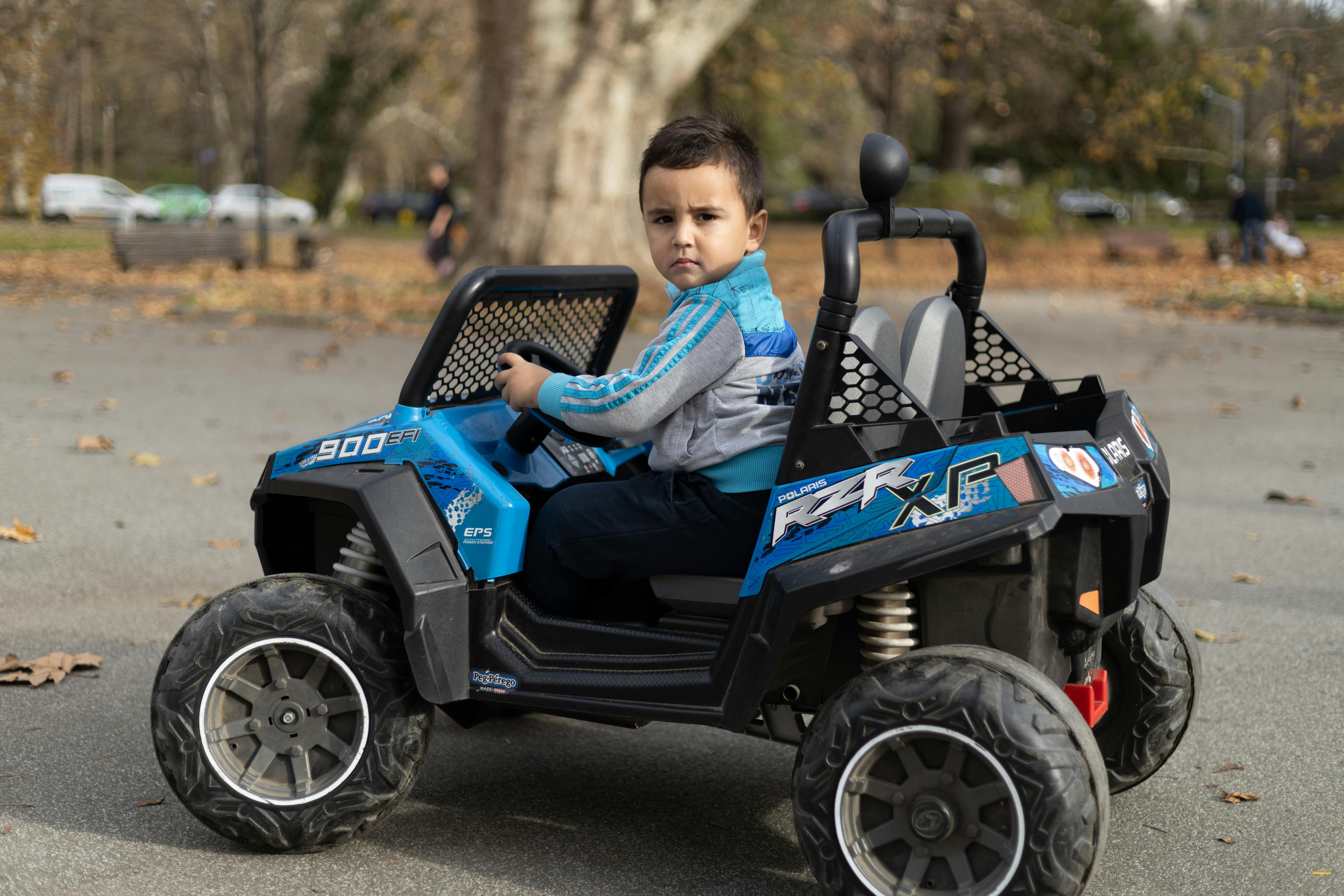 A child sitting and driving an electric toy car in a park. Outdoor fun and playtime.