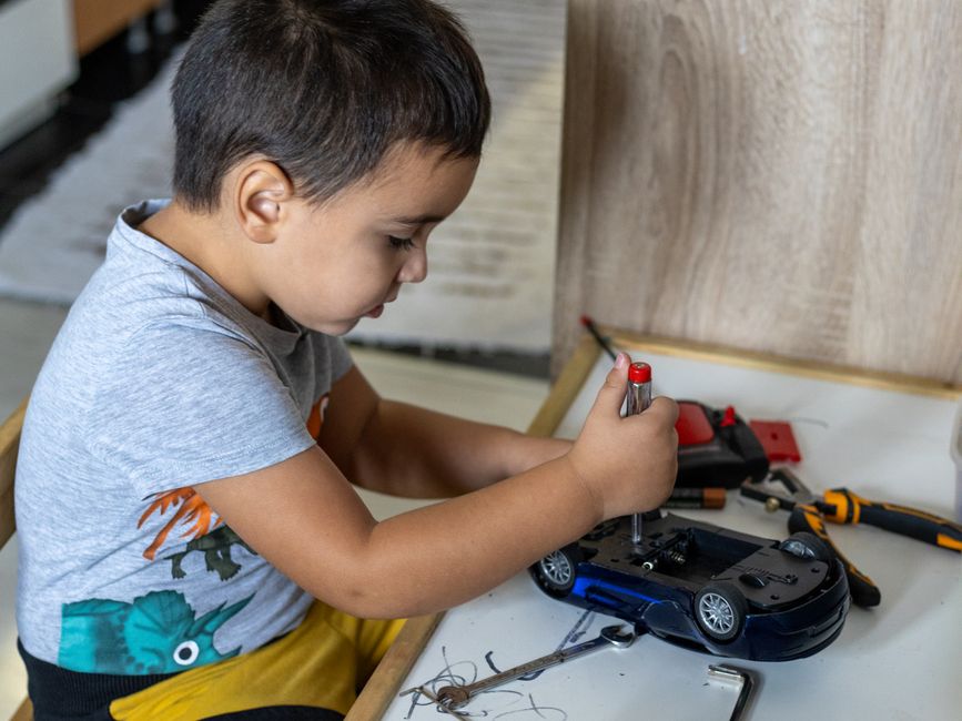 A young boy focused on assembling a toy car using tools indoors, showcasing creativity and learning.