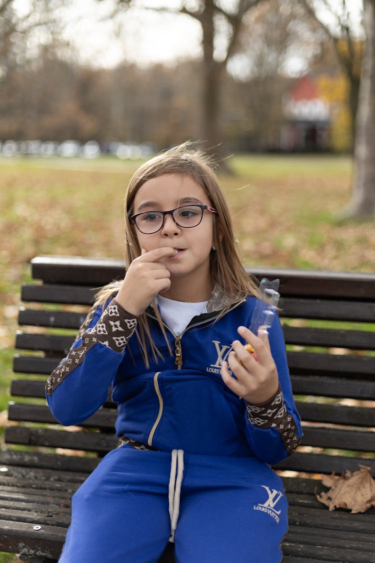 Child In Louis Vuitton Blue Tracksuit Eating Sweets On A Park Bench