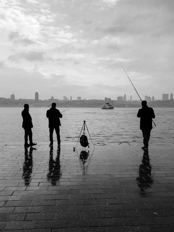 Three people standing on the shore with a fishing pole · Free Stock Photo