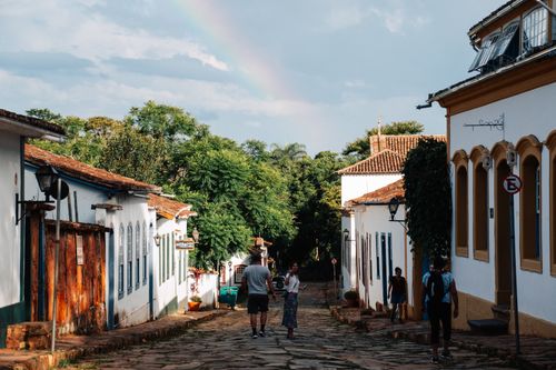 Free Scenic view of people walking on a cobblestone street in Tiradentes with colonial buildings and a rainbow. Stock Photo