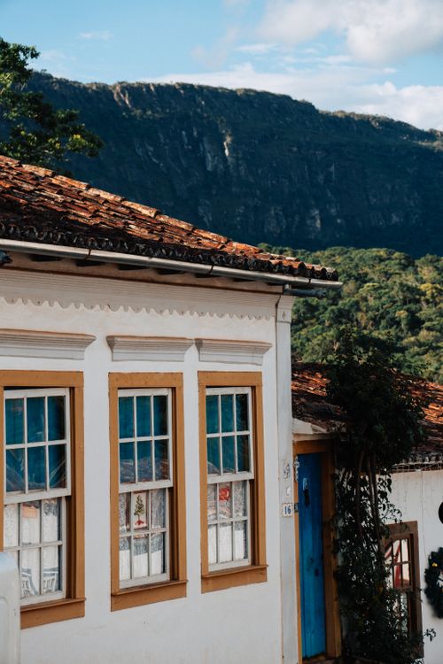 Free White colonial house with red roof and mountains in background, capturing the essence of rustic architecture. Stock Photo