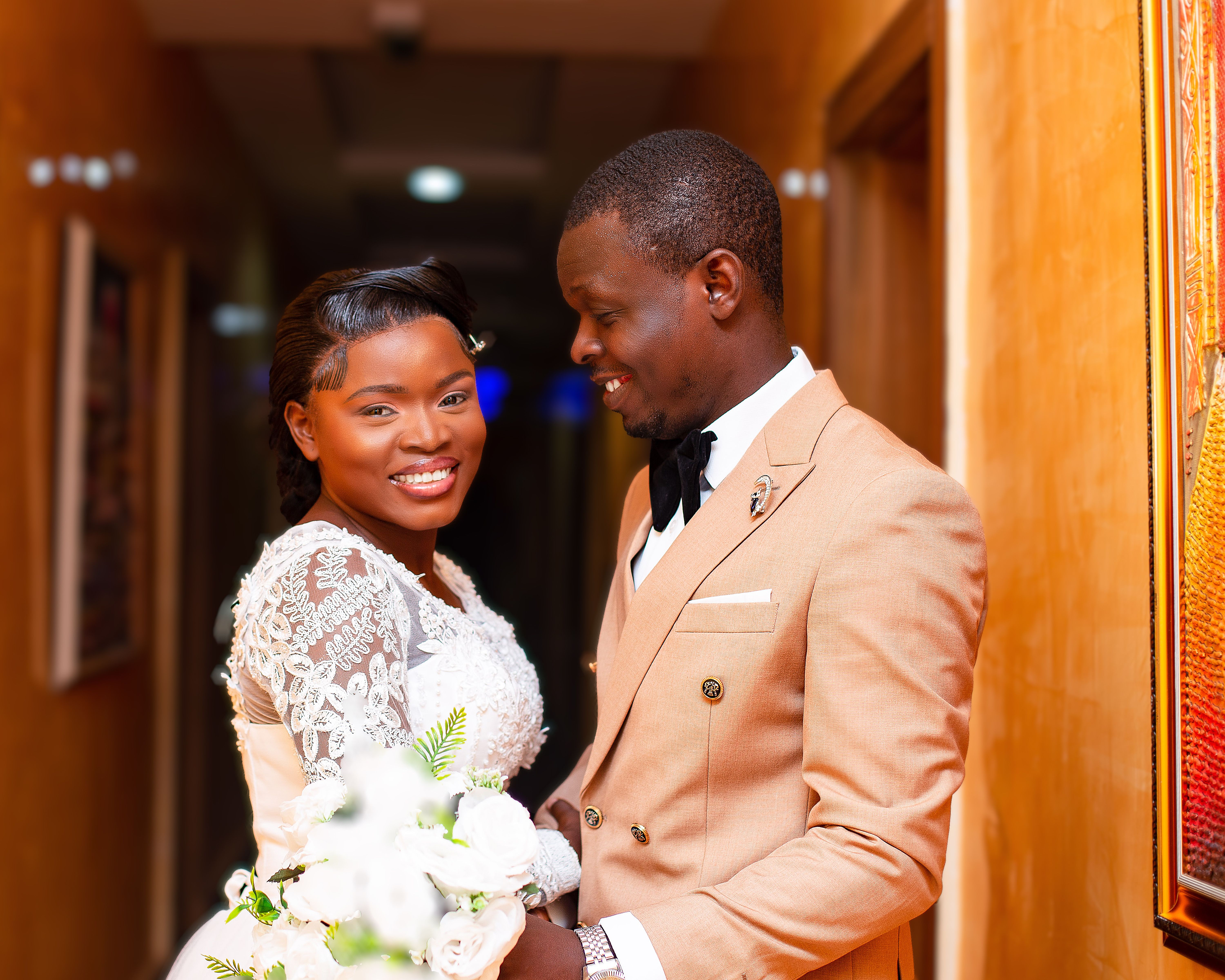 Joyful newlywed couple in a corridor, elegantly dressed and smiling.