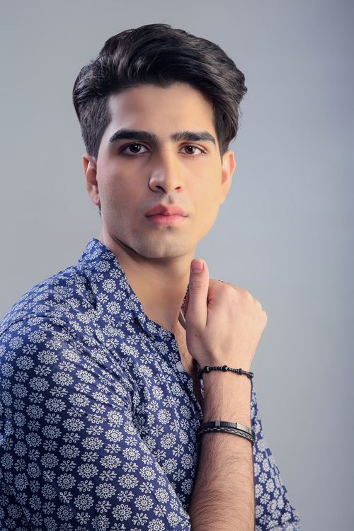 Free Portrait of a stylish young man in a studio, showcasing elegance and fashion with a gray background. Stock Photo