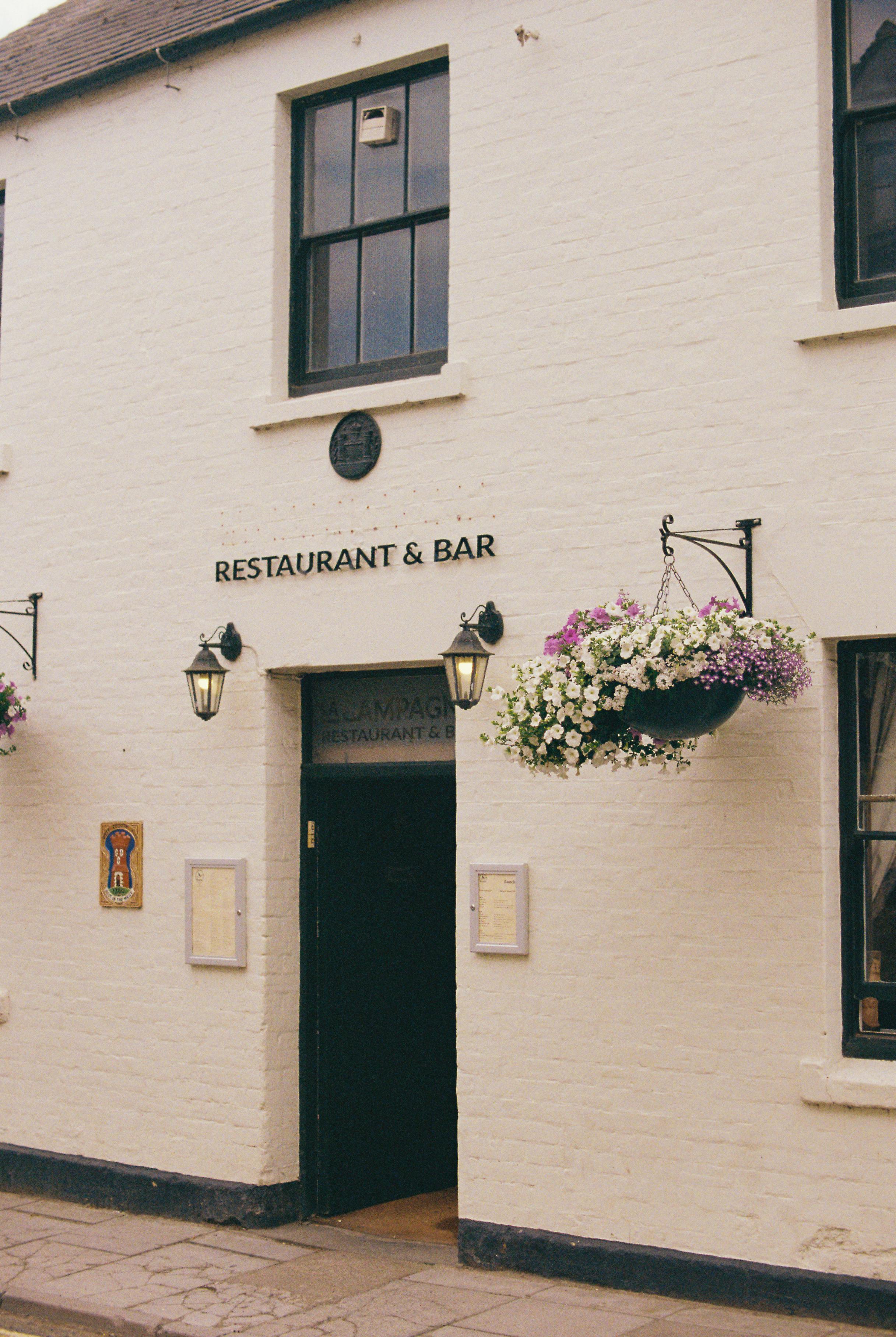 Elegant entrance of a vintage restaurant and bar adorned with hanging flowers.