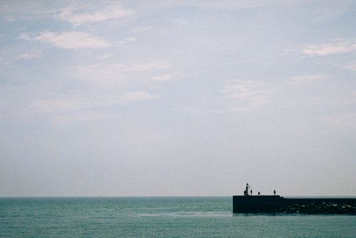 Free A tranquil ocean scene with a jetty and people enjoying a quiet moment under a bright sky. Stock Photo