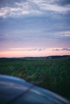 Scenic view of green countryside fields under a colorful dusk sky.