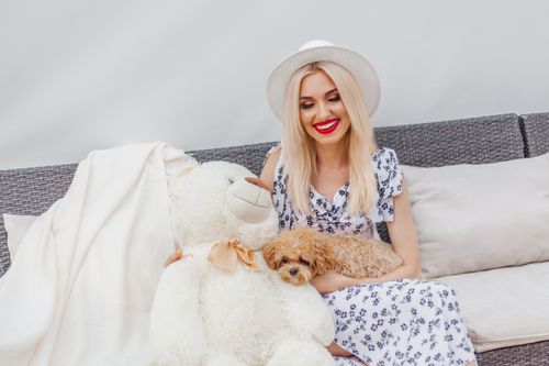 Free Smiling woman relaxing indoors with a plush teddy bear and small fluffy dog, embodying warmth and relaxation. Stock Photo