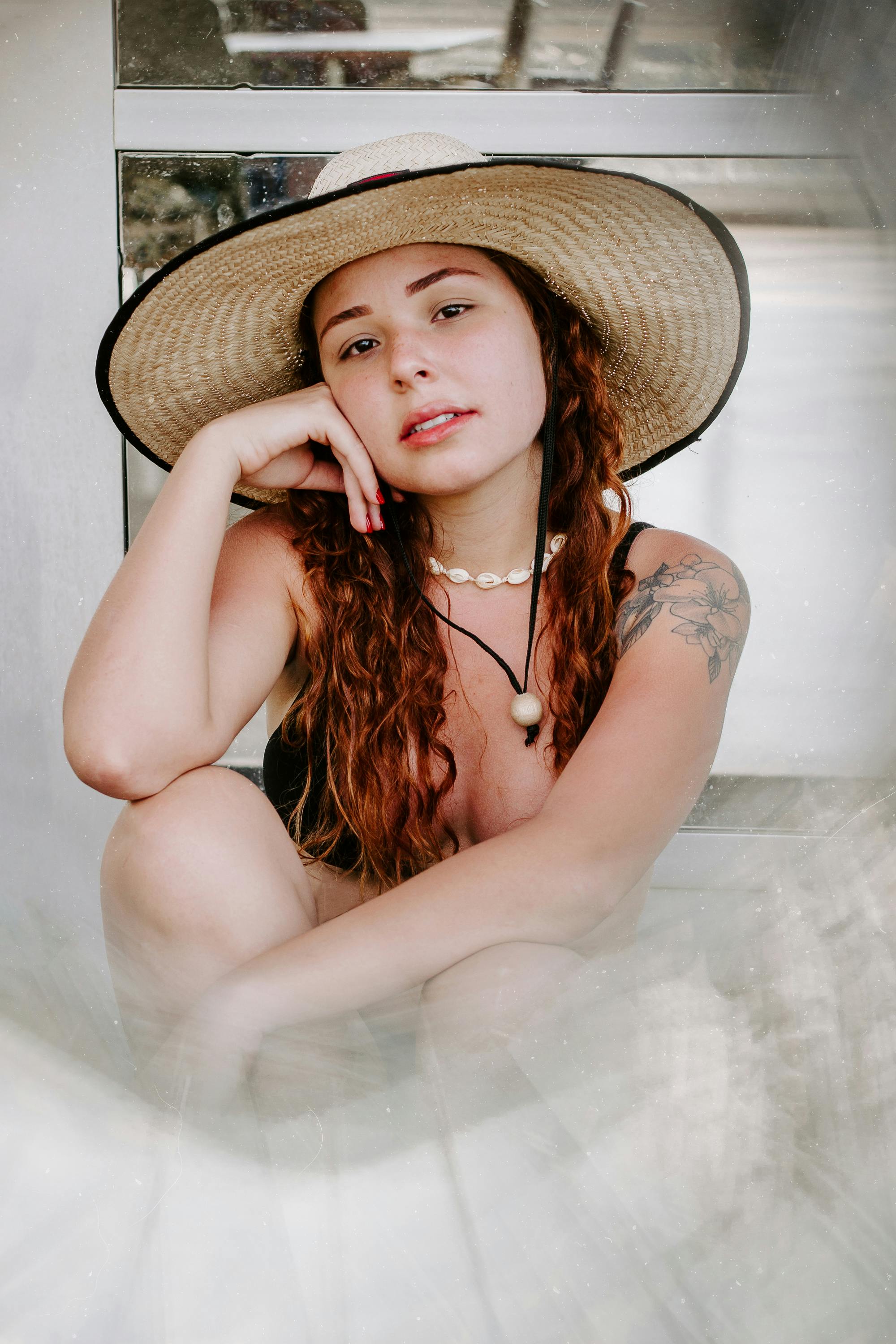 woman in bikini and straw hat sitting on sand