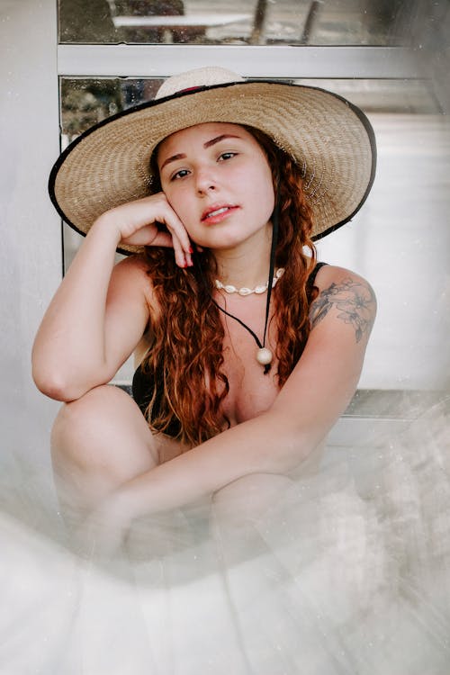 бесплатная Женщина в бикини и соломенной шляпе сидит на песке Стоковое фото