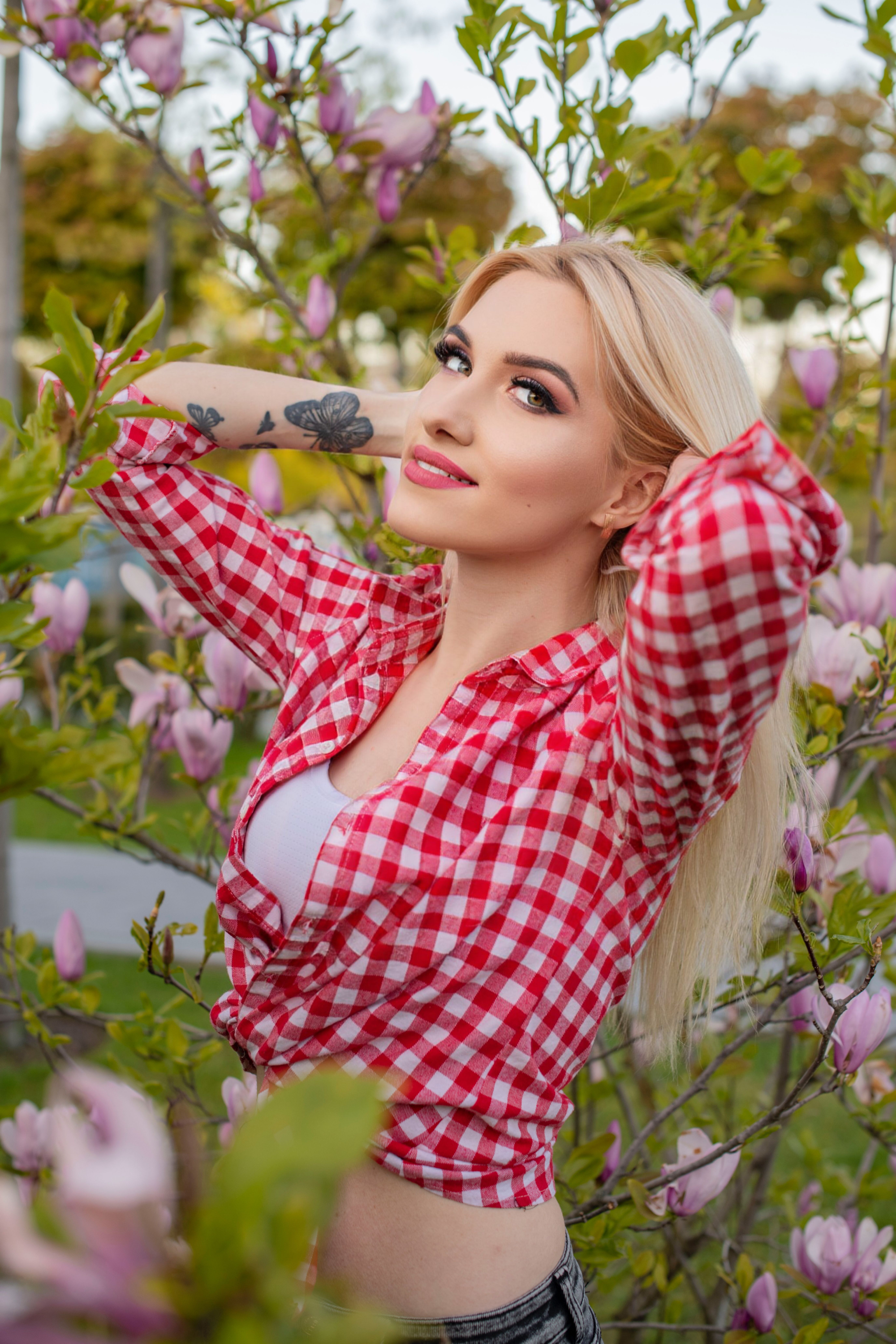 Blonde woman in checkered shirt enjoys a sunny day in a blooming garden.