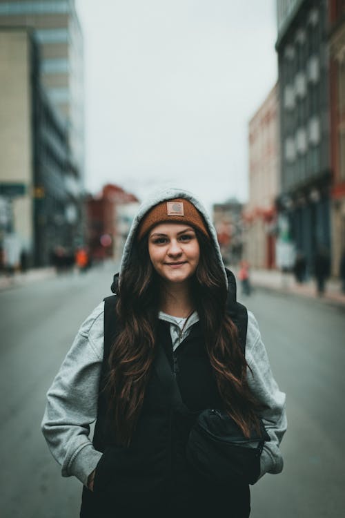 Young Woman in Hoodie and Vest Posing in Middle of Street