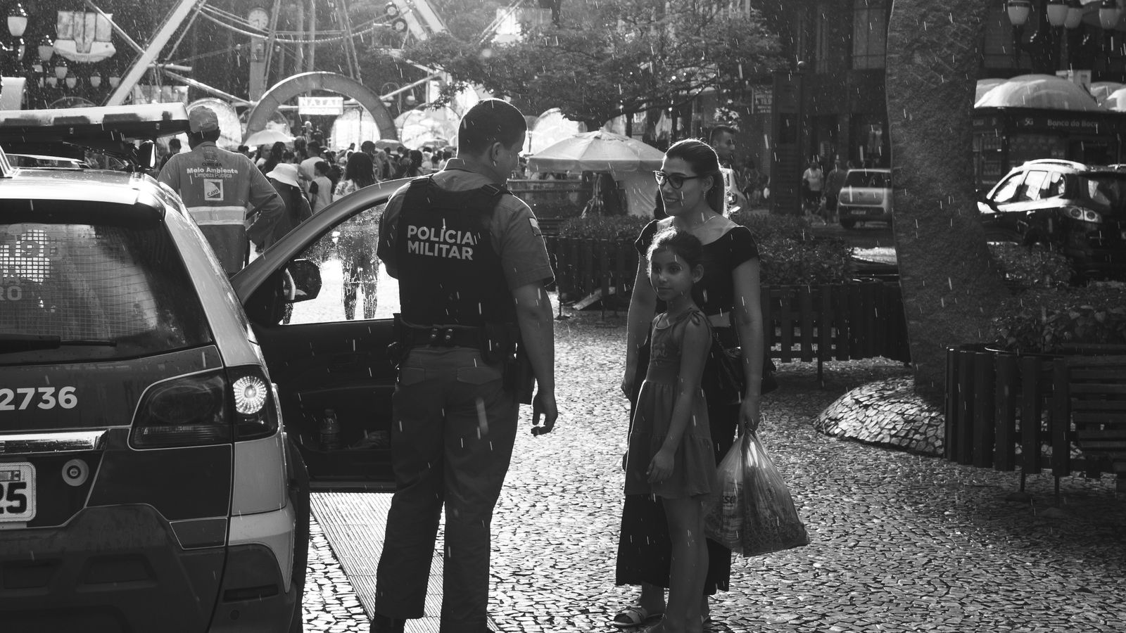 Black and white image of a police officer interacting with a family on a rainy street.