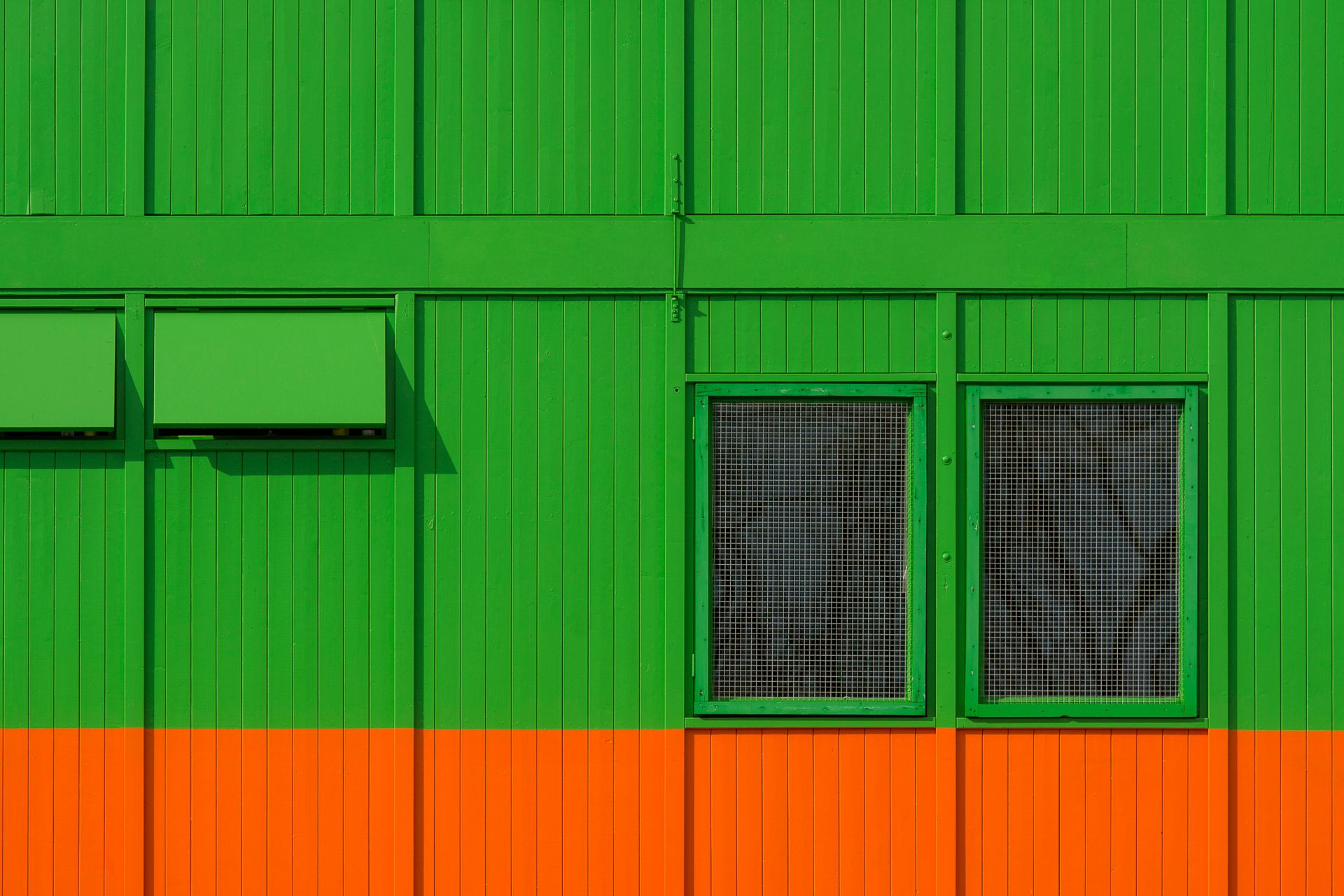 Bright green and orange building facade with two windows and geometric design.