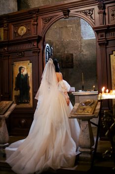 A bride in a wedding dress stands in a beautifully ornate church setting, surrounded by icons.